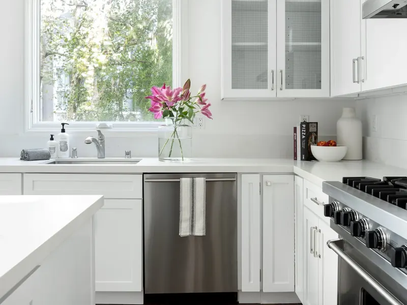 White kitchen with clear worktops, sink under the window and stainless steel dishwasher