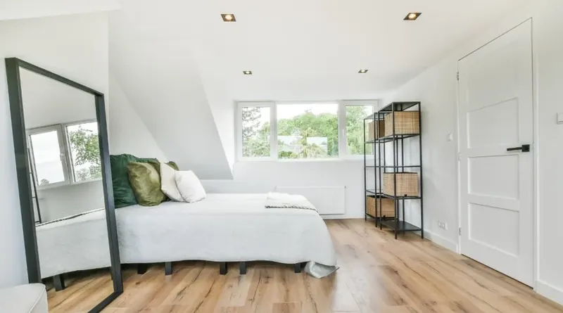 Bright loft bedroom with a made bed, wooden floor and tall mirror