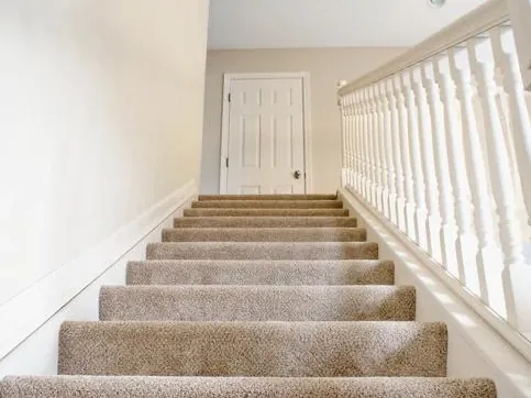 Carpeted staircase with white banister leading to a landing